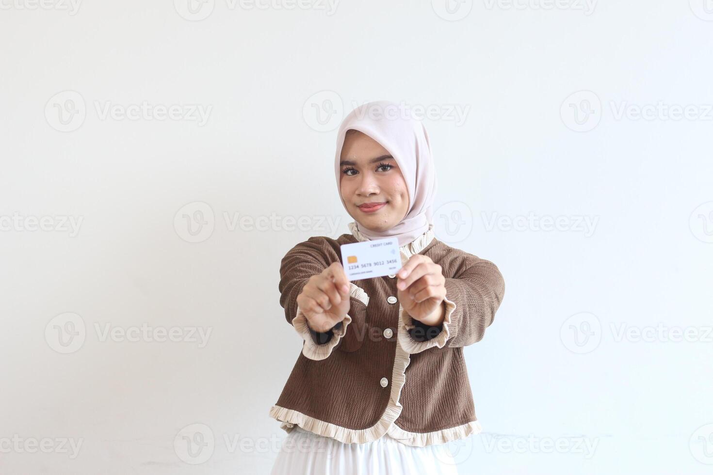 Smiling Muslim Woman in Brown Cardigan Holding Credit Card Against White Background photo