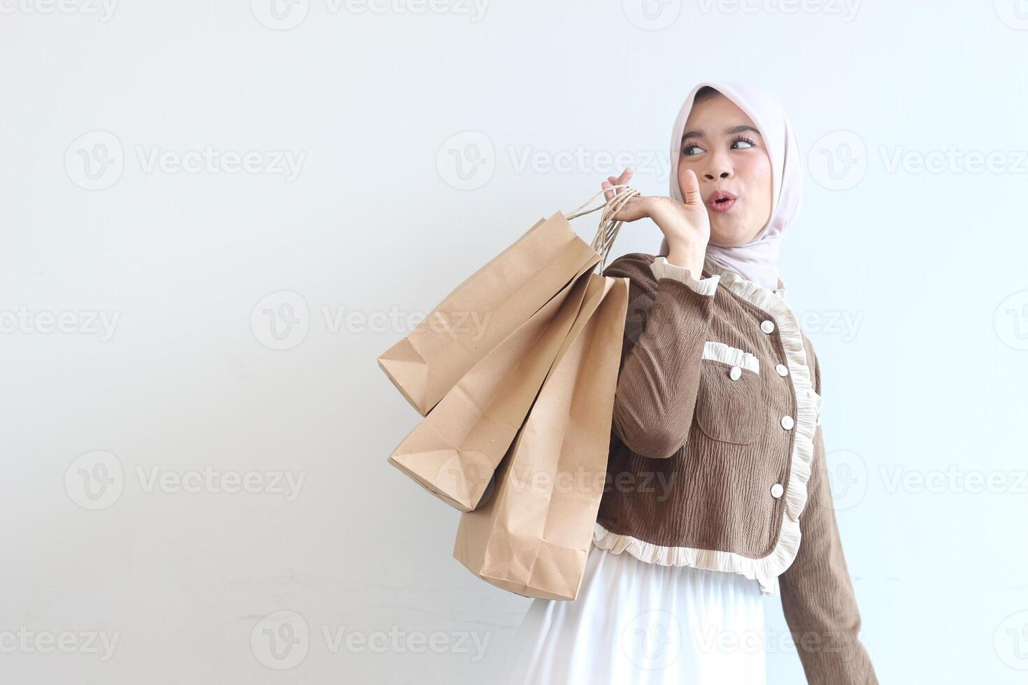 A Young Woman in a Brown Jacket and Hijab Holds Shopping Bags Against a White Background photo