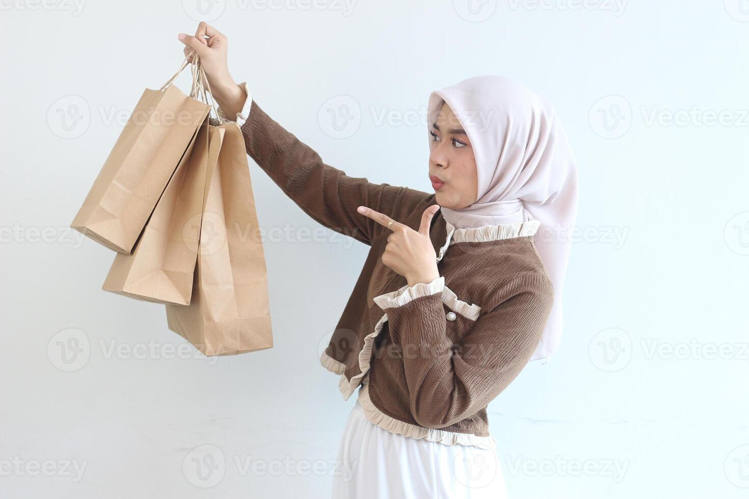 A Muslim Woman in Brown Outfit Showing Off Her Paper Shopping Bags Against a White Background photo