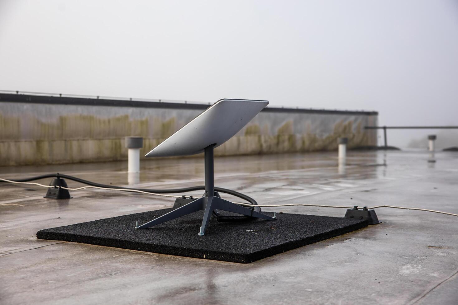 Sigulda Latvia, 2024 - Satellite Dish on Wet Rooftop with Overcast Sky and Mossy Wall photo