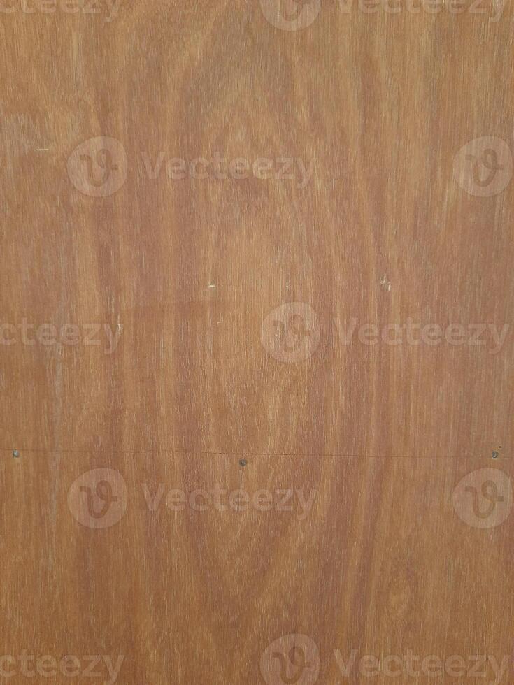 a wooden surface featuring a natural wood grain pattern. The wood has a medium-brown tone with visible horizontal lines, small nail marks, and subtle texture, giving it a raw and organic appearance. photo