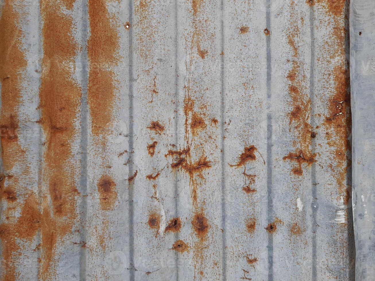 a close-up view of a textured surface a metal sheet, with a dull grayish tone. The surface features a mix of light and dark patches, creating a mottled, weathered, or oxidized appearance photo