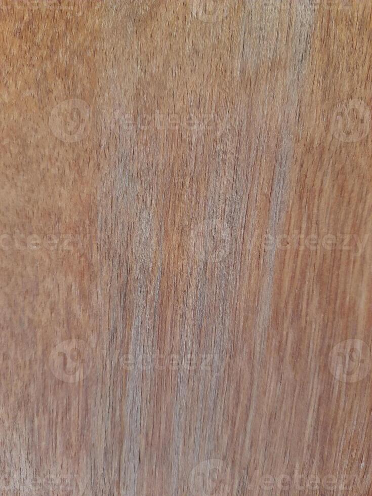 a wooden surface featuring a natural wood grain pattern. The wood has a medium-brown tone with visible horizontal lines, small nail marks, and subtle texture, giving it a raw and organic appearance. photo