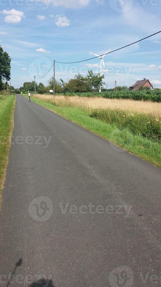 Beautiful and Scenic Country Road with a Cyclist Riding Near Expansive Green Fields photo