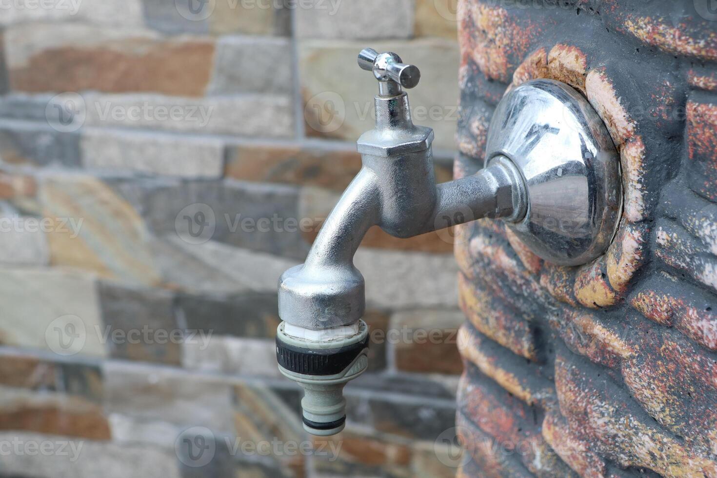 A modern outdoor faucet on a rustic stone wall, enhancing the gardens beauty and utility photo