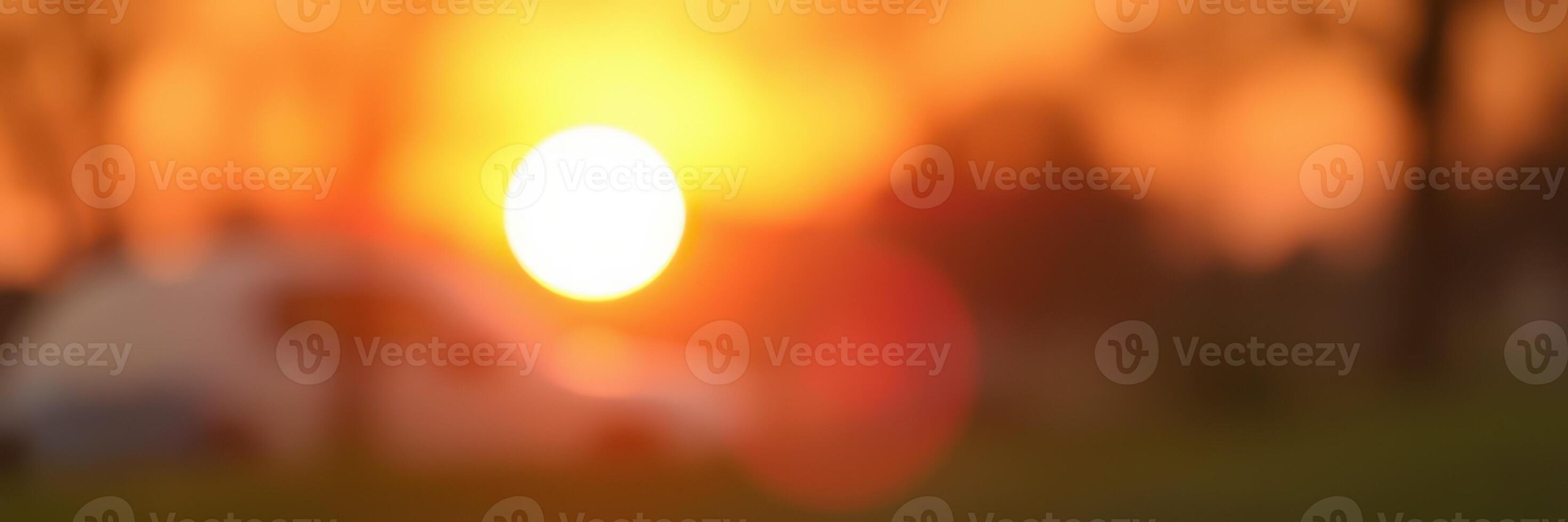 Sunset casting warm hues over a serene landscape with silhouettes of trees and a distant vehicle photo