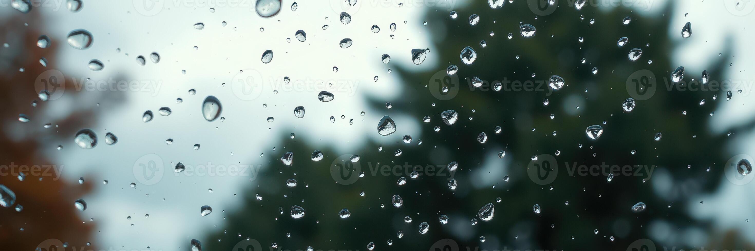 Raindrops collect on a window while trees sway gently in the background during a cloudy day photo