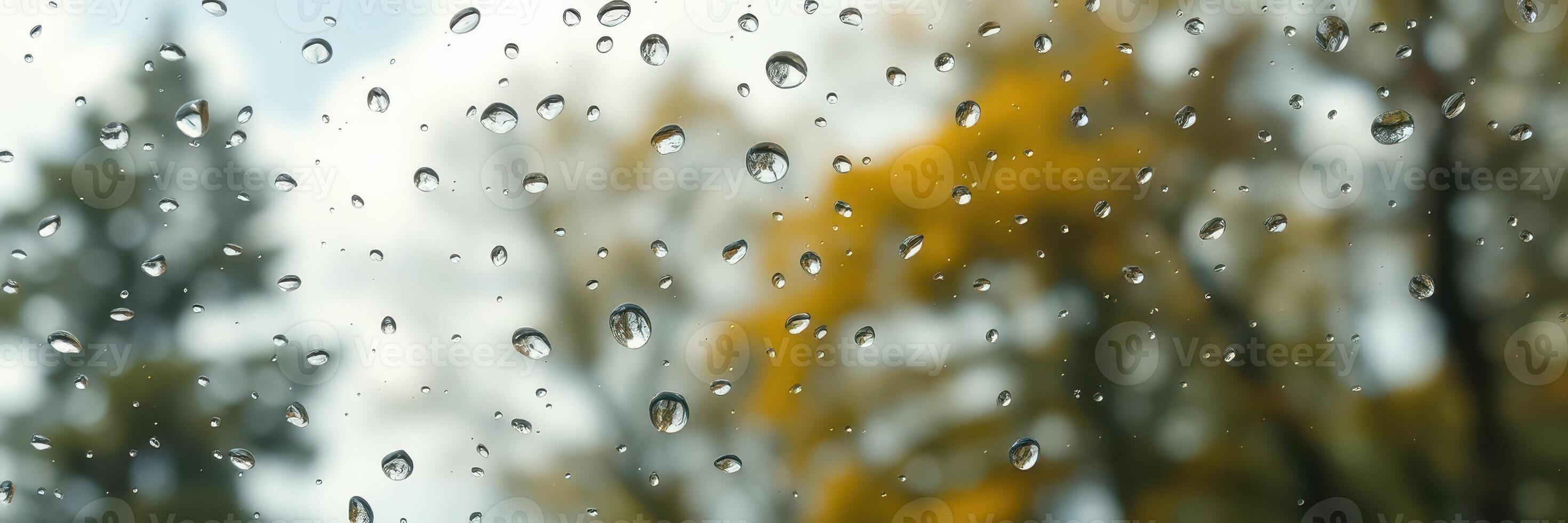 Raindrops on windowpane with autumn trees blurred in the background during a cloudy day photo