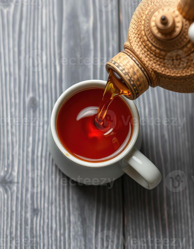 Brewed tea pours into a white cup on rustic wood surface in a cozy setting photo