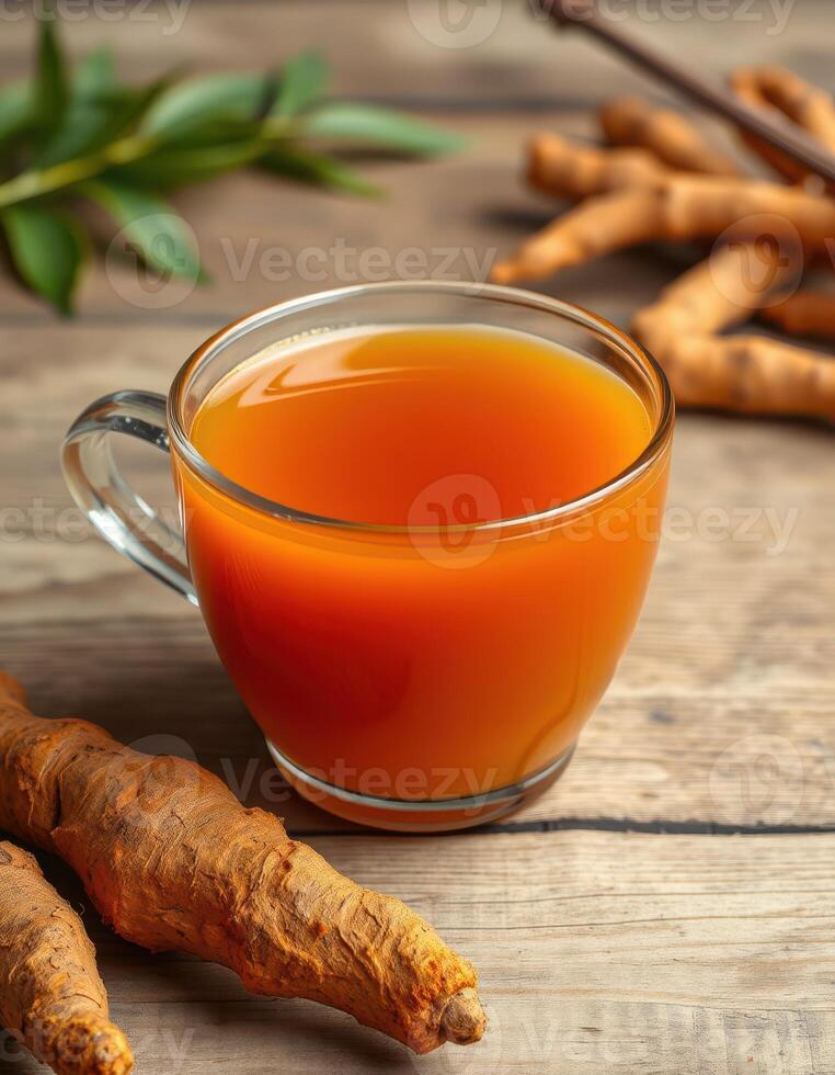 Turmeric tea served in a clear glass cup with fresh roots on a wooden table photo
