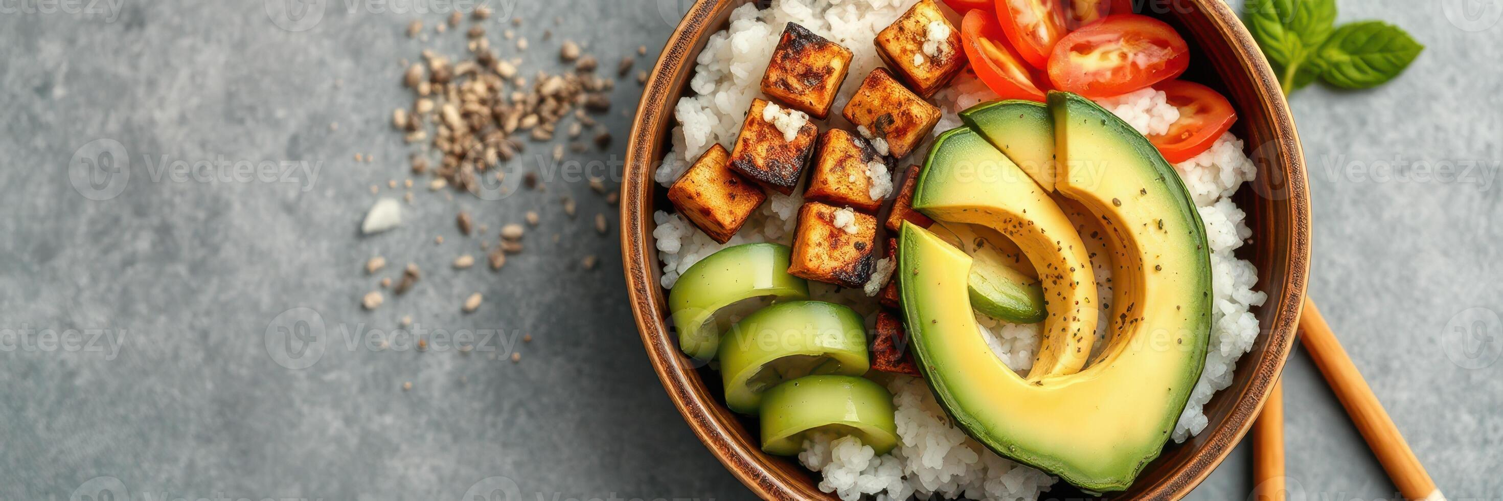 Colorful vegan rice bowl with grilled tofu, fresh vegetables, and avocado on a textured surface photo