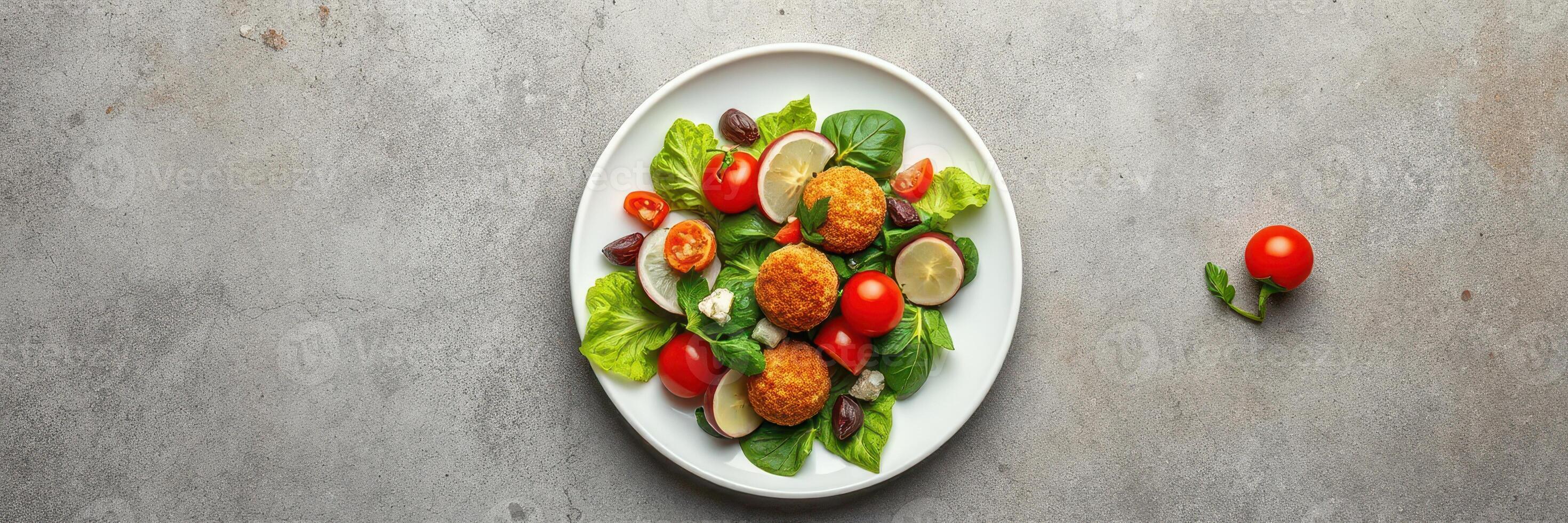 Fresh salad with crispy falafel, cherry tomatoes, and lime served in a white bowl on a gray stone background photo