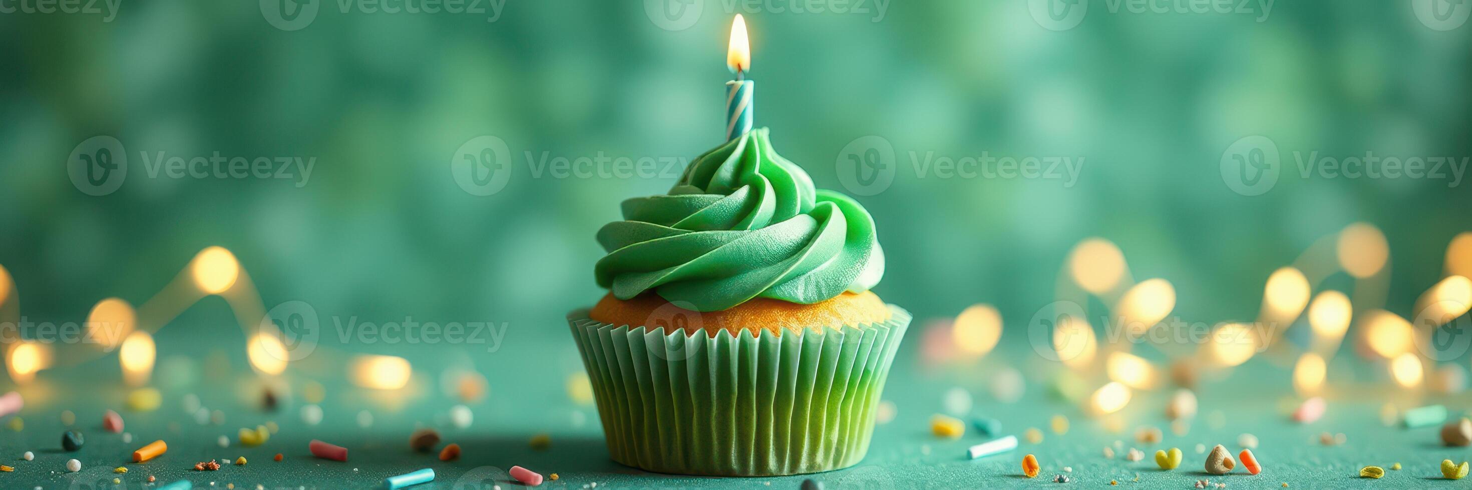 Colorful green cupcake with candle on a festive table decorated with sprinkles photo
