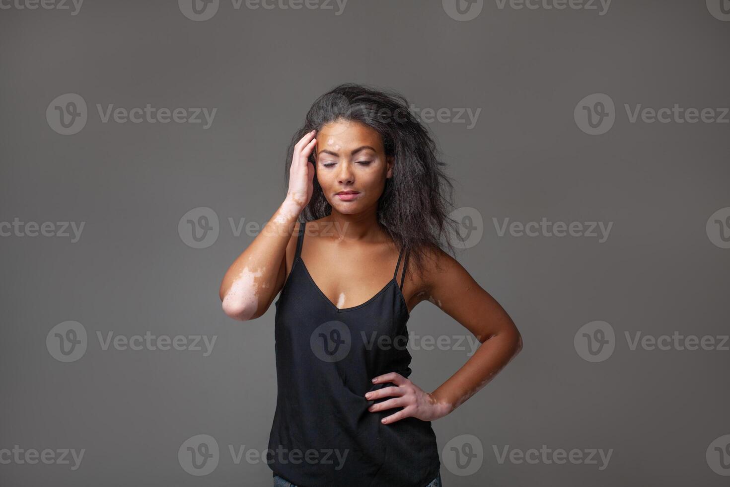 Sensuous female fashion model standing with hand on hip in gray studio photo
