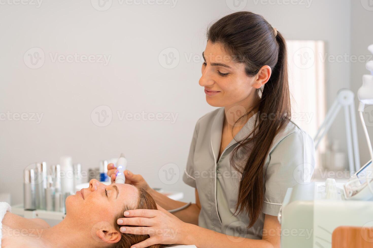 Smiling female cosmetologist applying iontophoresis on client's face photo
