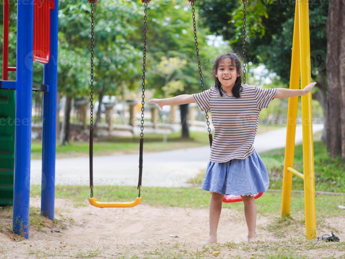 Cute girl having fun on the swing in the playground in the park. Children playing in the playground during summer vacation. photo
