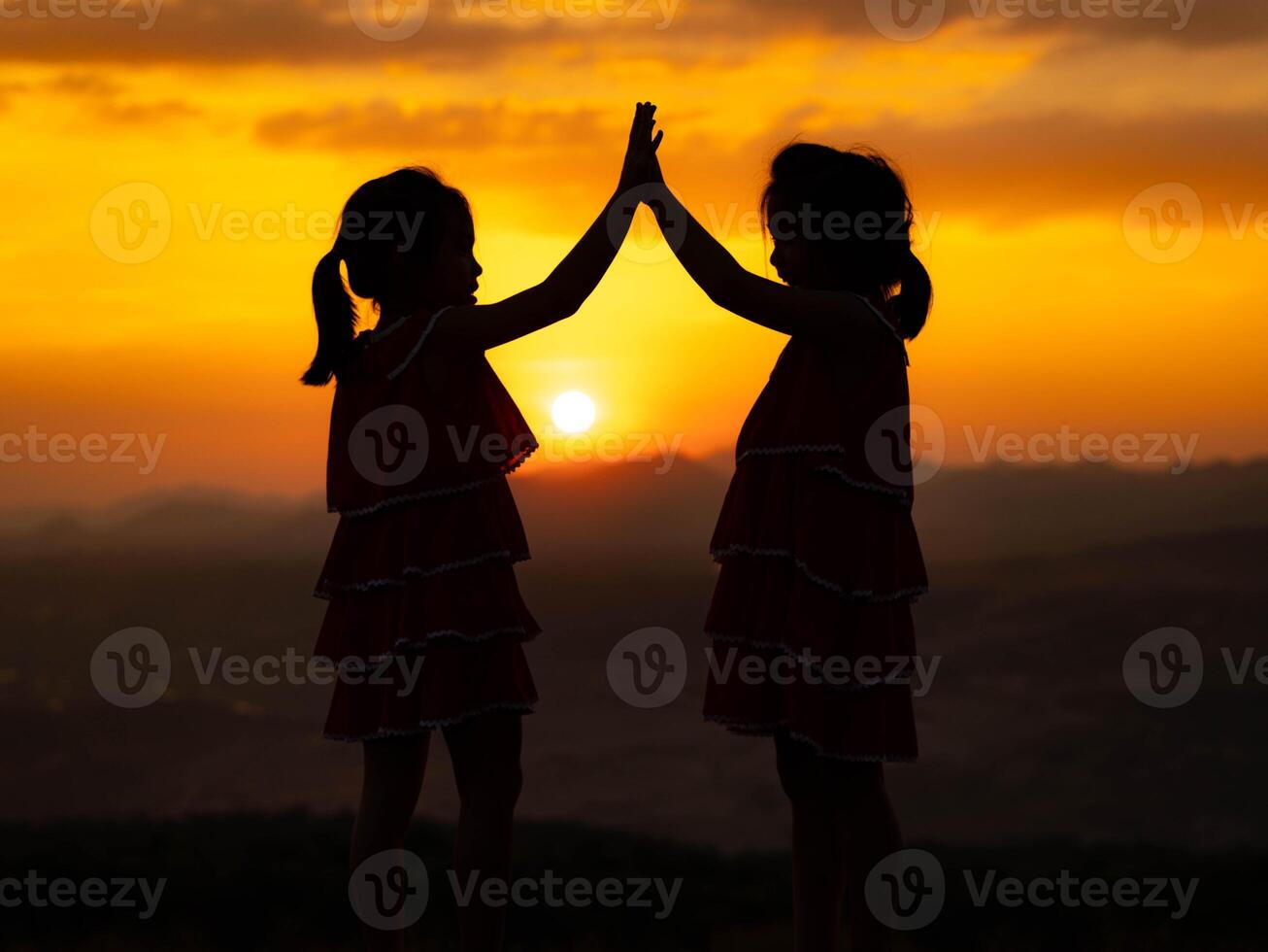 Silhouette of two little girls are happily playing on meadow during a summer sunset. Family love with colorful sunset. photo