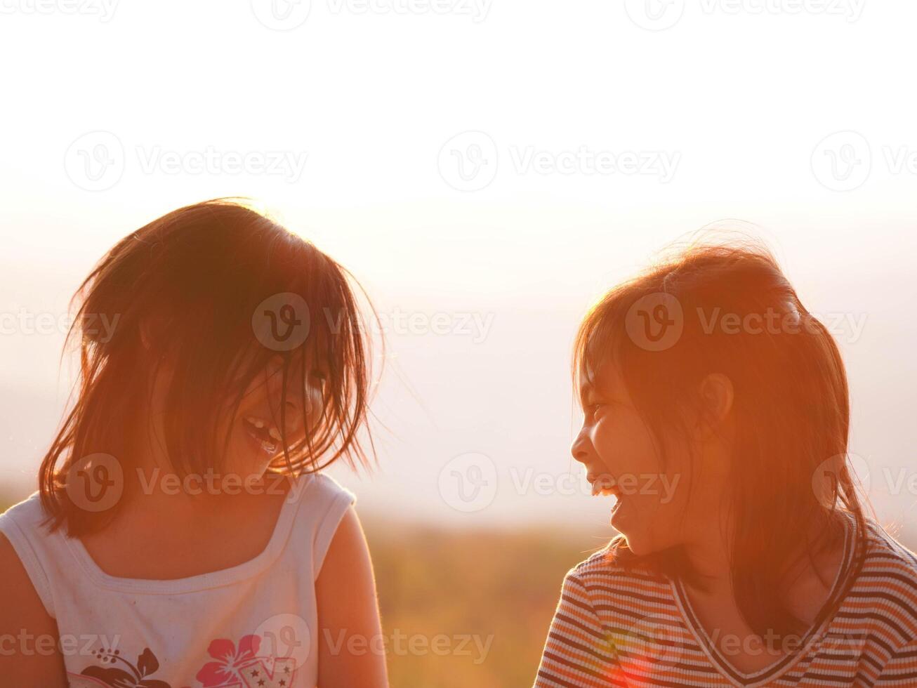 Two little girls are happily playing on meadow during a summer sunset. Family love with colorful sunset. photo