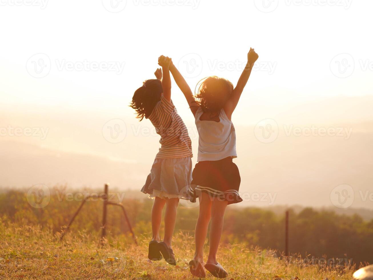 Two little girls are happily playing on meadow during a summer sunset. Family love with colorful sunset. photo