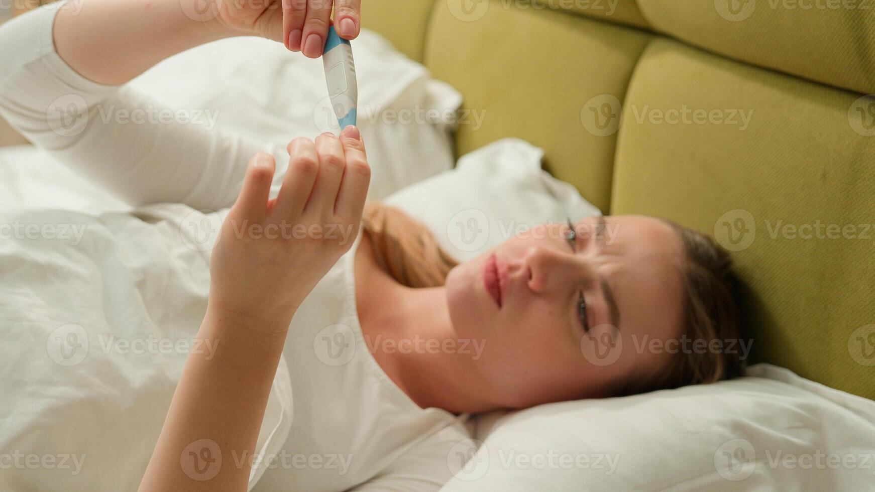 Ill sick unhealthy unwell Caucasian woman female girl at home bedroom lying bed suffer with disease symptoms check temperature fever with thermometer sneeze sneezing cold flue medicine health problem photo