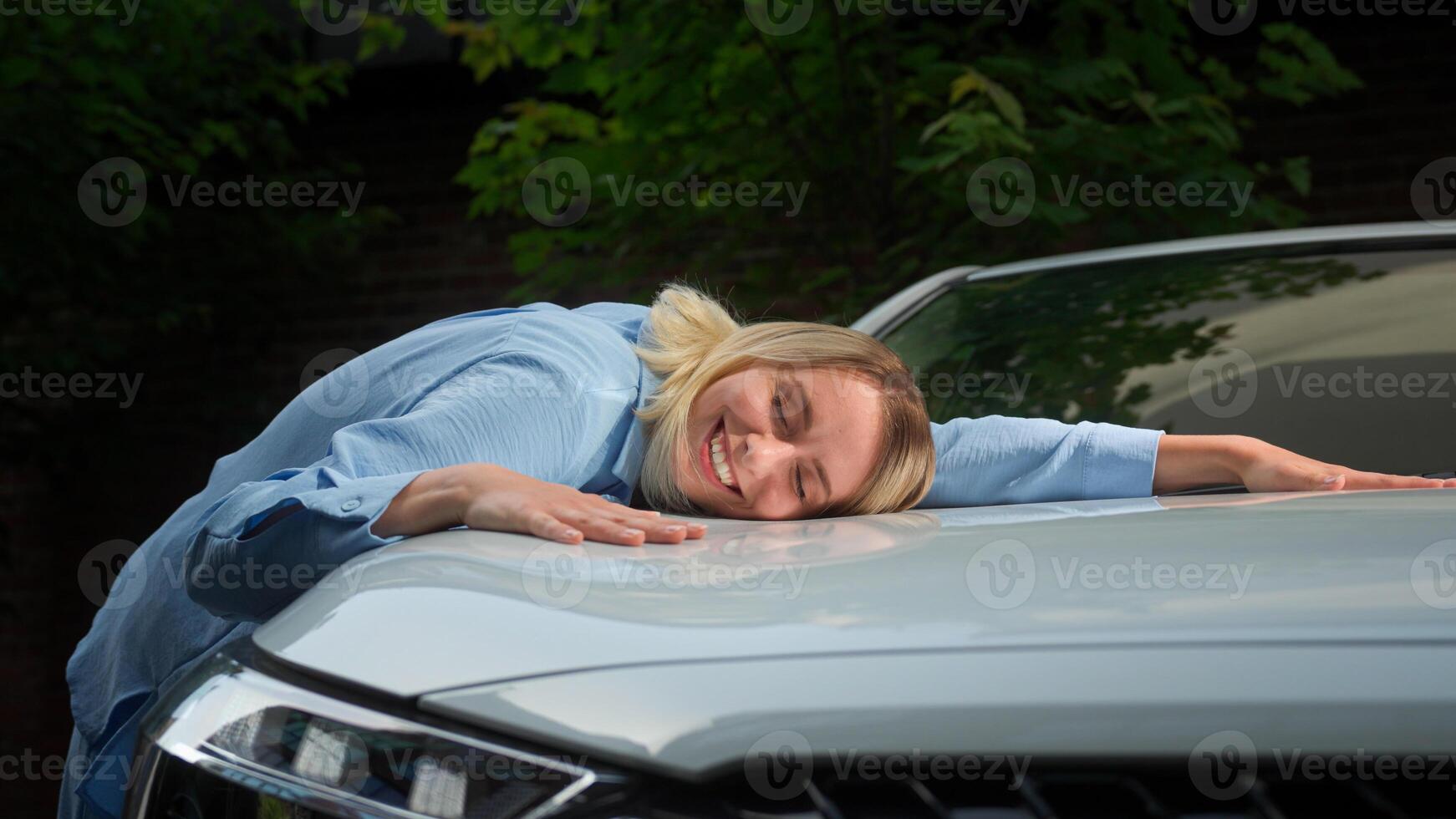 Satisfied positive Caucasian businesswoman machine automobile owner girl smile driver lying on car in city transport rent lady rejoicing new vehicle client woman buy touch female embracing luxury auto photo