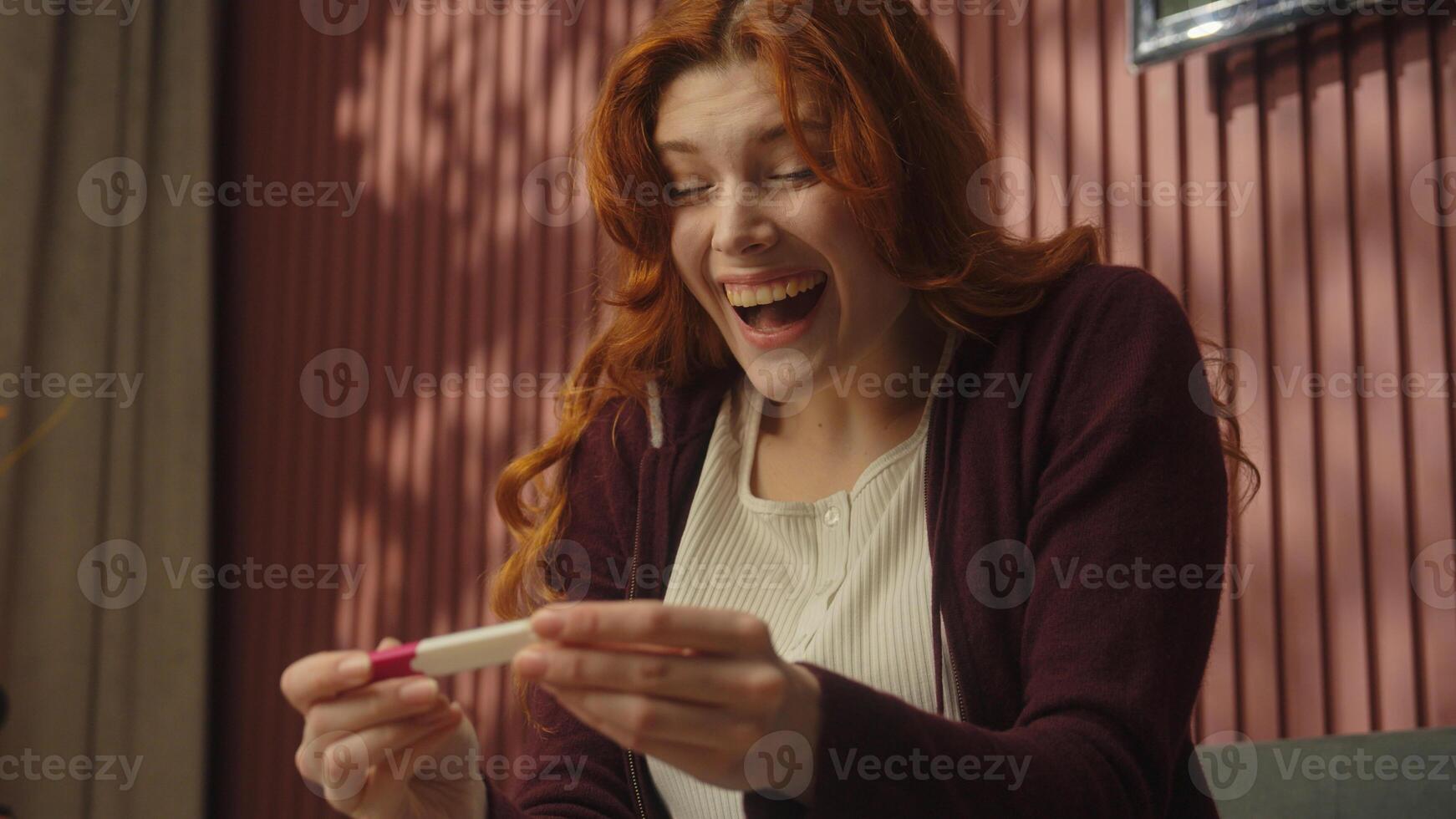 Caucasian happy excited woman on home couch shocked girl future mom mother hold pregnancy test positive result rejoice scream emotions female fertility treatment IVF expect wait baby birth celebrate photo