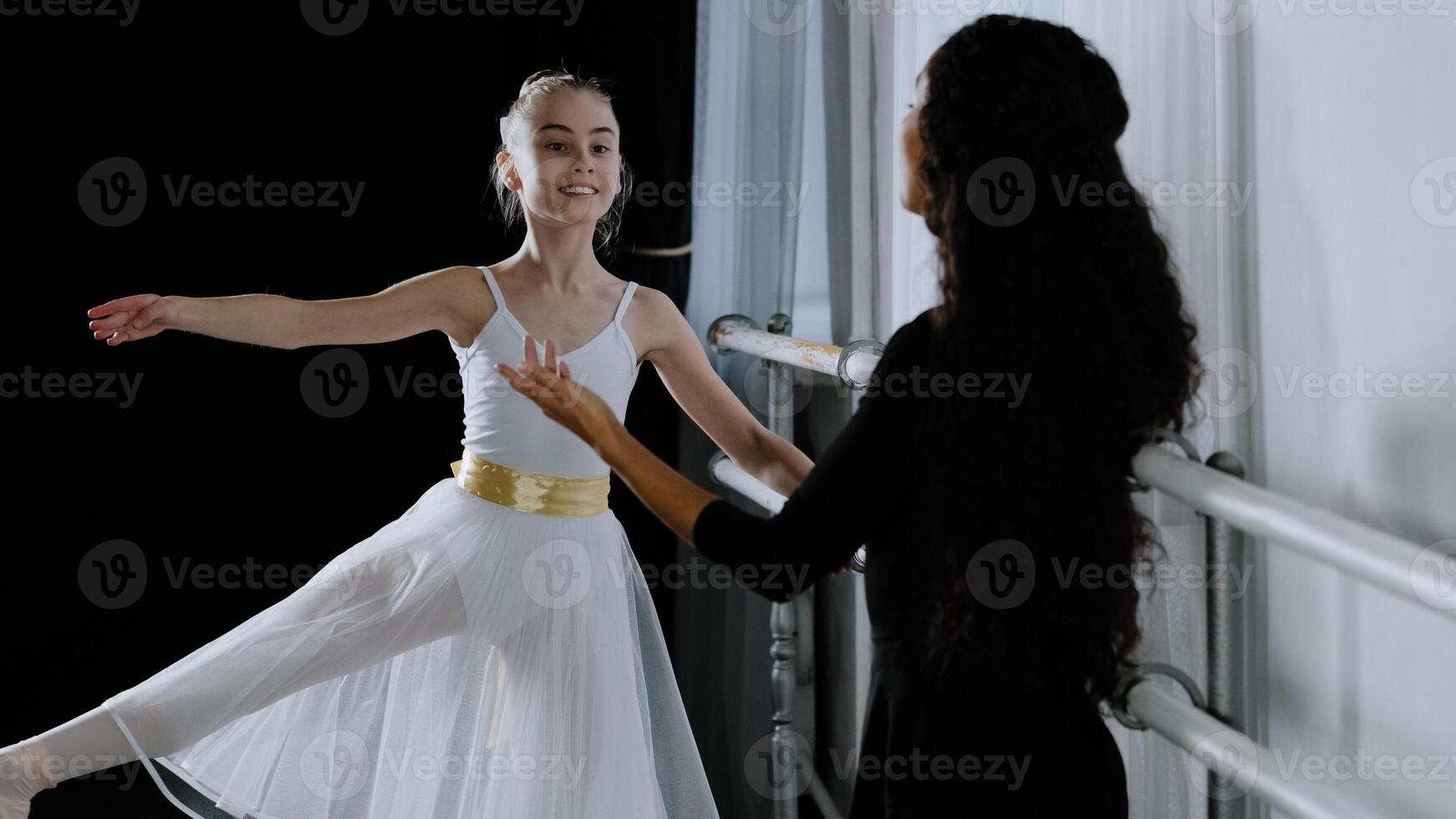 Caucasian girl teenager student ballerina in tutu doing dancing exercises near ballet barre listening to explanations advice from adult teacher female trainer rehearsing choreography dance education photo