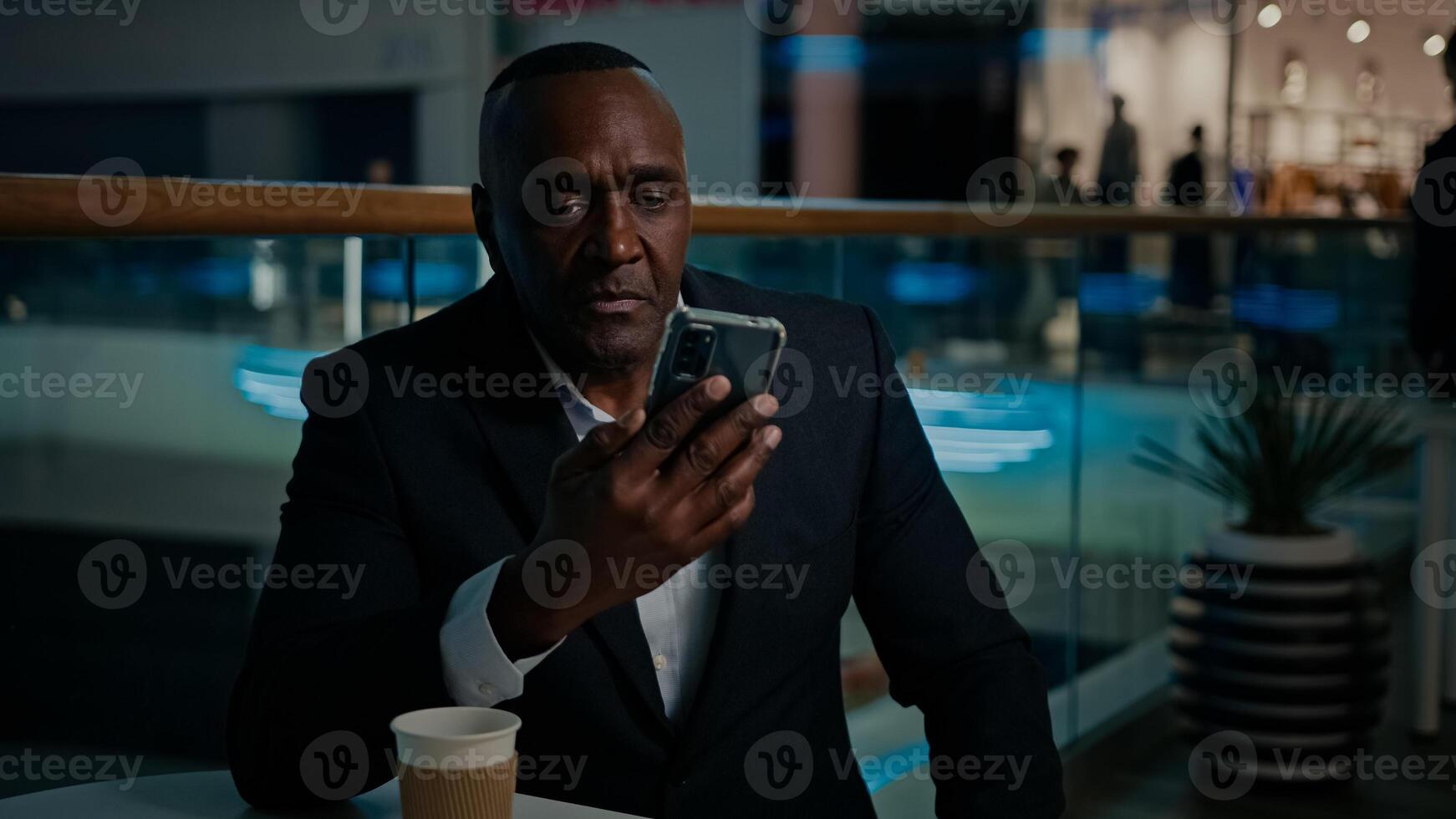 50s Ethnic African American man entrepreneur middle-aged businessman talk call with mobile phone conference answer no dissatisfied talking with cellphone with business colleague sitting in cafe photo