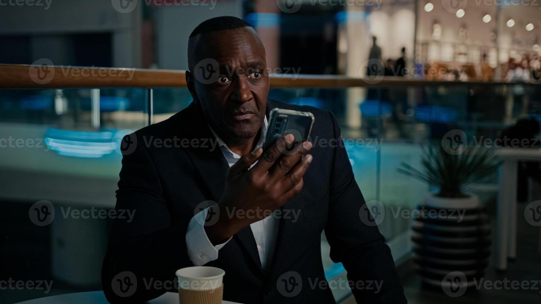 Adult Ethnic African American man entrepreneur middle-aged businessman talk call with mobile phone conference answer no dissatisfied talking with cellphone with business colleague sit in cafe photo