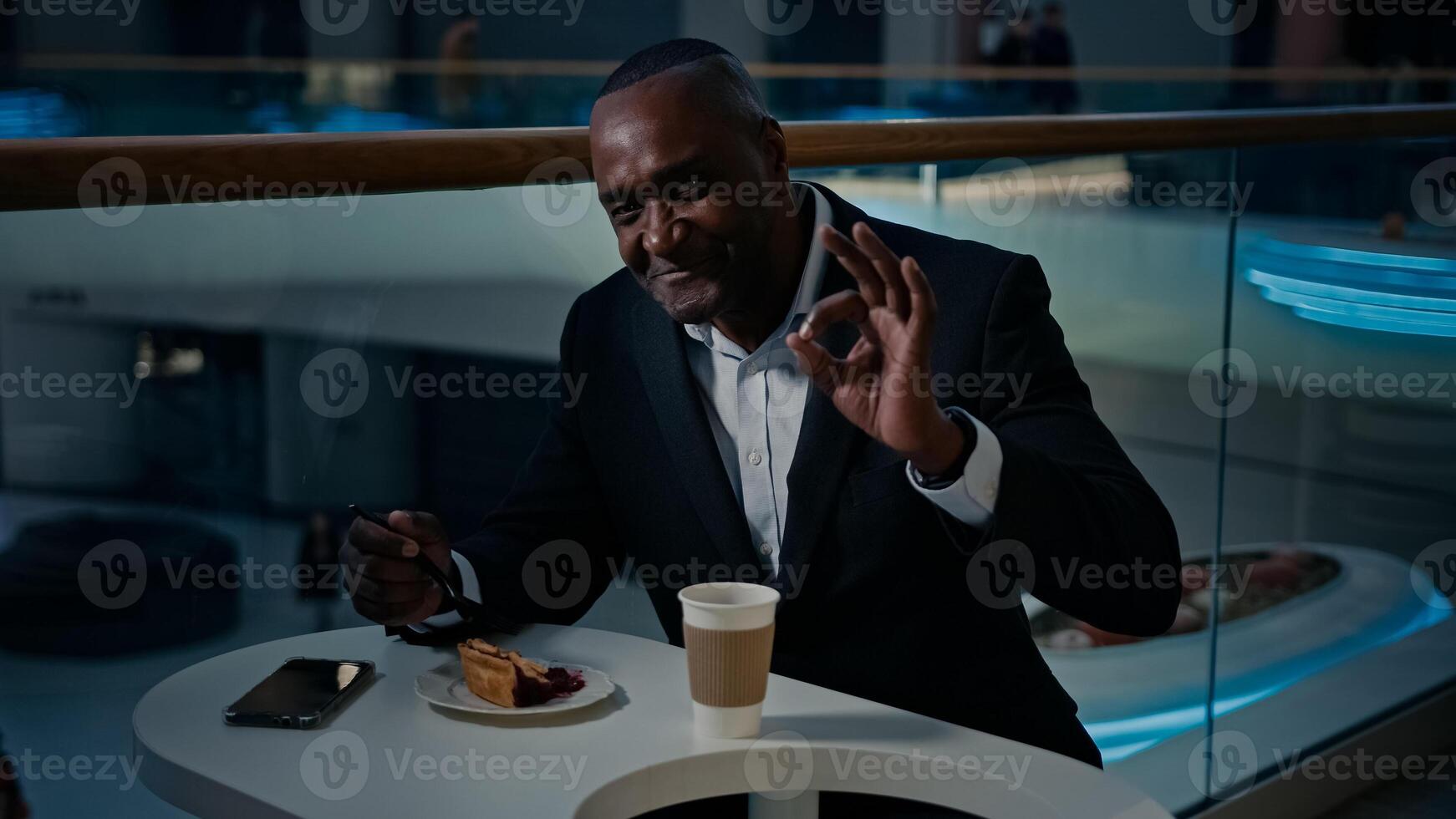 Ethnic African American middle-aged businessman entrepreneur man visitor sitting at cafe table eating pie good tasty cake dessert showing thumb up ok okay gesture recommend satisfied in restaurant photo