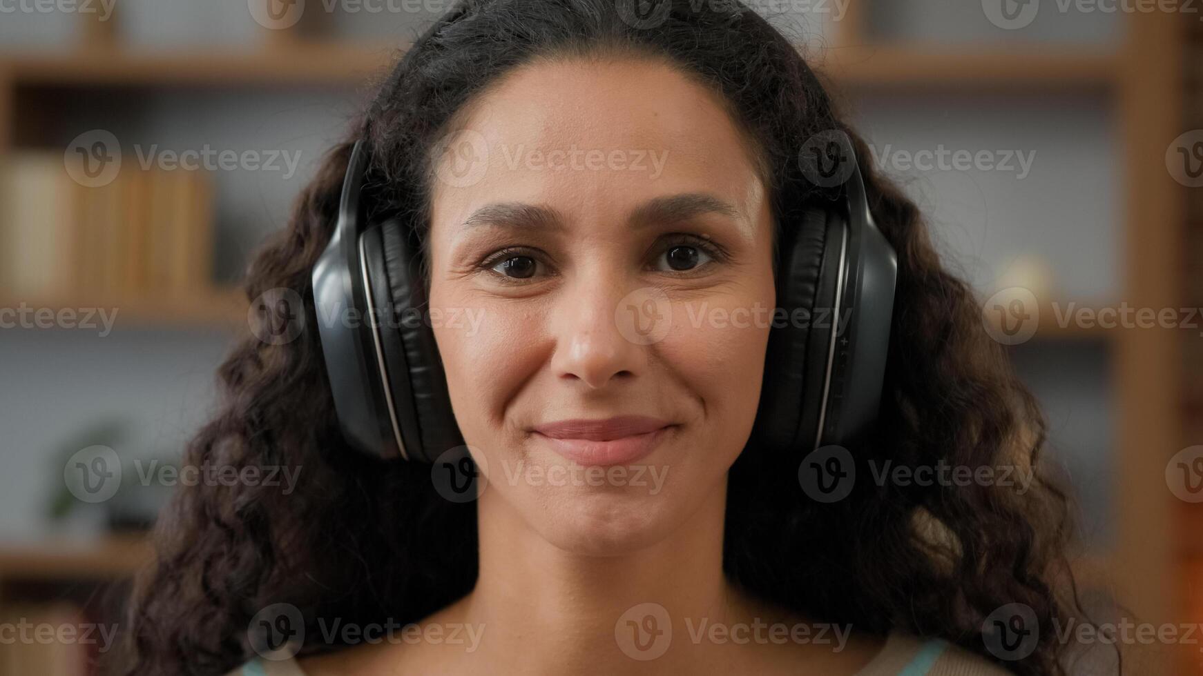 Portrait smiling carefree cheerful Hispanic Latino Caucasian 30s woman looking at camera with smile enjoy audio sound wearing headphones relaxing having fun listening music melody at home weekend photo