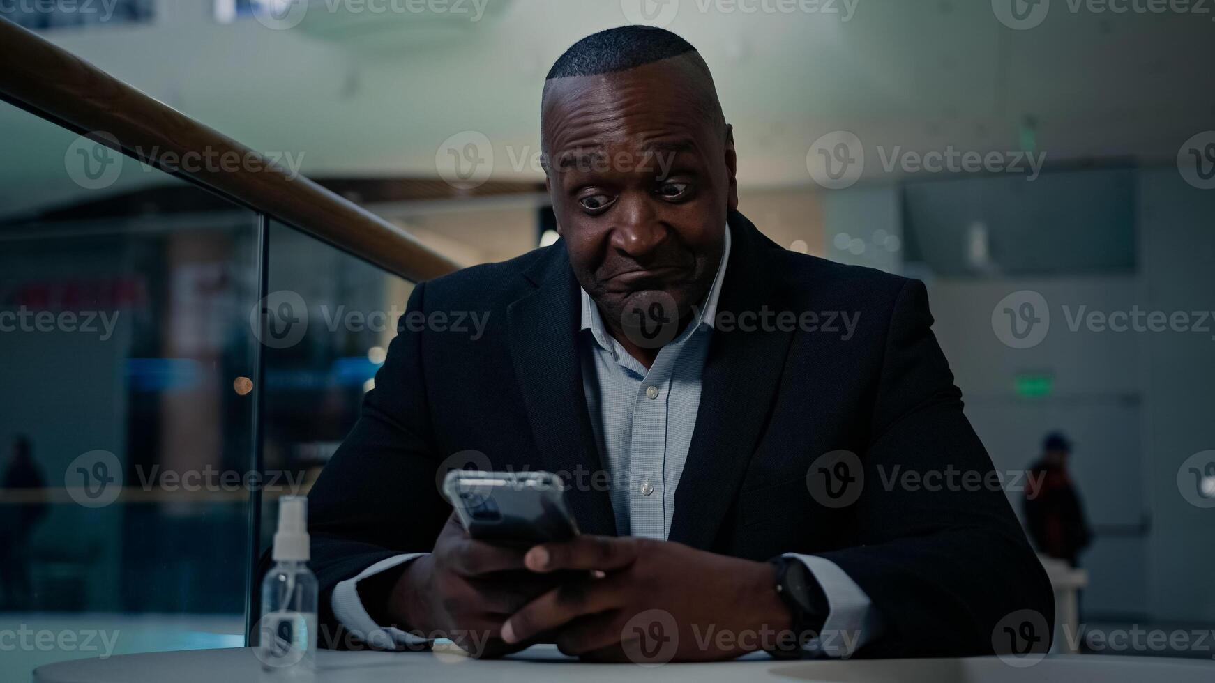 African American adult middle-aged mature man employee businessman indoors in office cafe table looking phone typing chatting texting mobile message online business chat browsing smartphone thinking photo