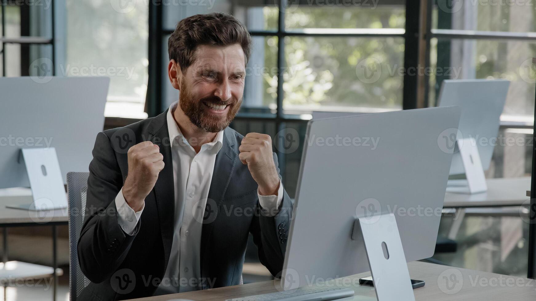 Exited happy Caucasian bearded businessman in office looking at computer with emotion winner cheerful rejoice with online win financial betting growth man worker CEO overjoyed celebrating success photo