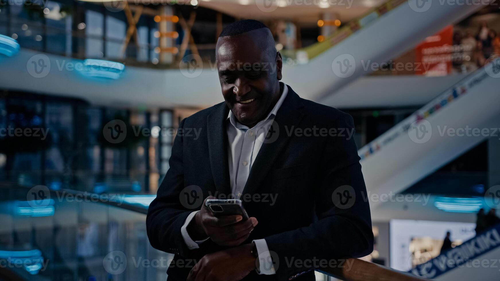 African American businessman standing in shopping mall company office man looking at mobile phone talk has call smartphone conference talking discussing friendly smile answer cellphone chat photo
