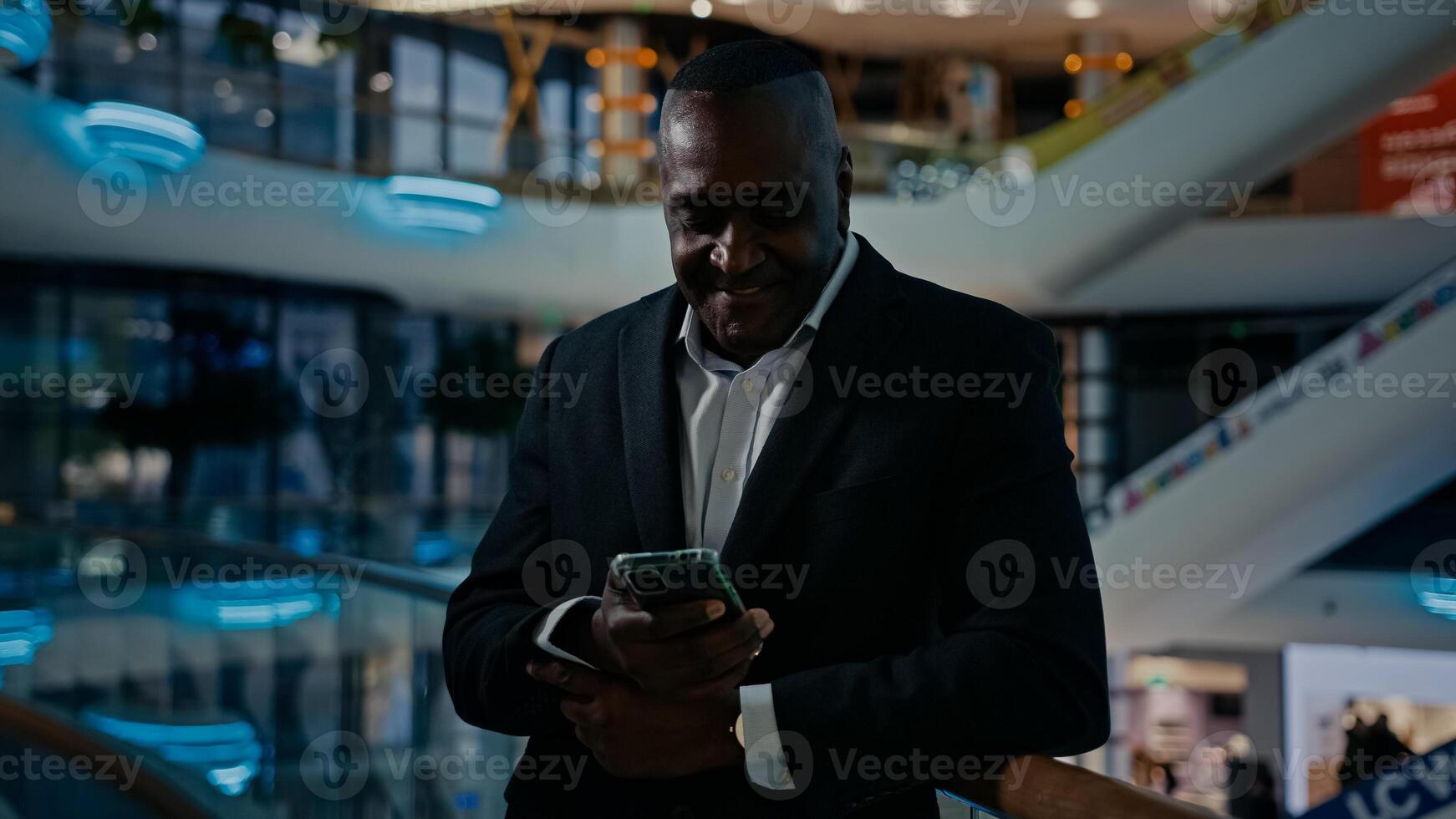 African American businessman standing in shopping mall company office looking at mobile phone screen talk has call smartphone conference talking discussing friendly smile answer cellphone chat photo