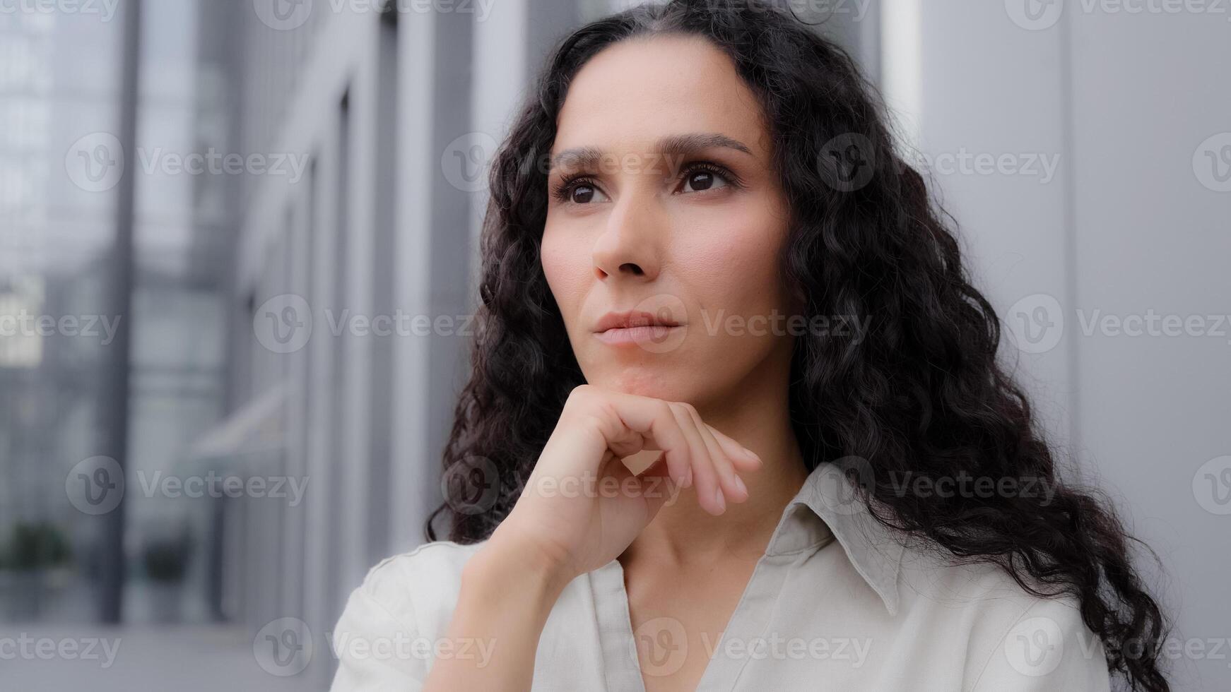Close up pensive thoughtful puzzled Caucasian Hispanic thoughtfully girl woman with curly hair standing outdoors sad worry dreaming planning businesswoman thinking about idea solution problem thought photo