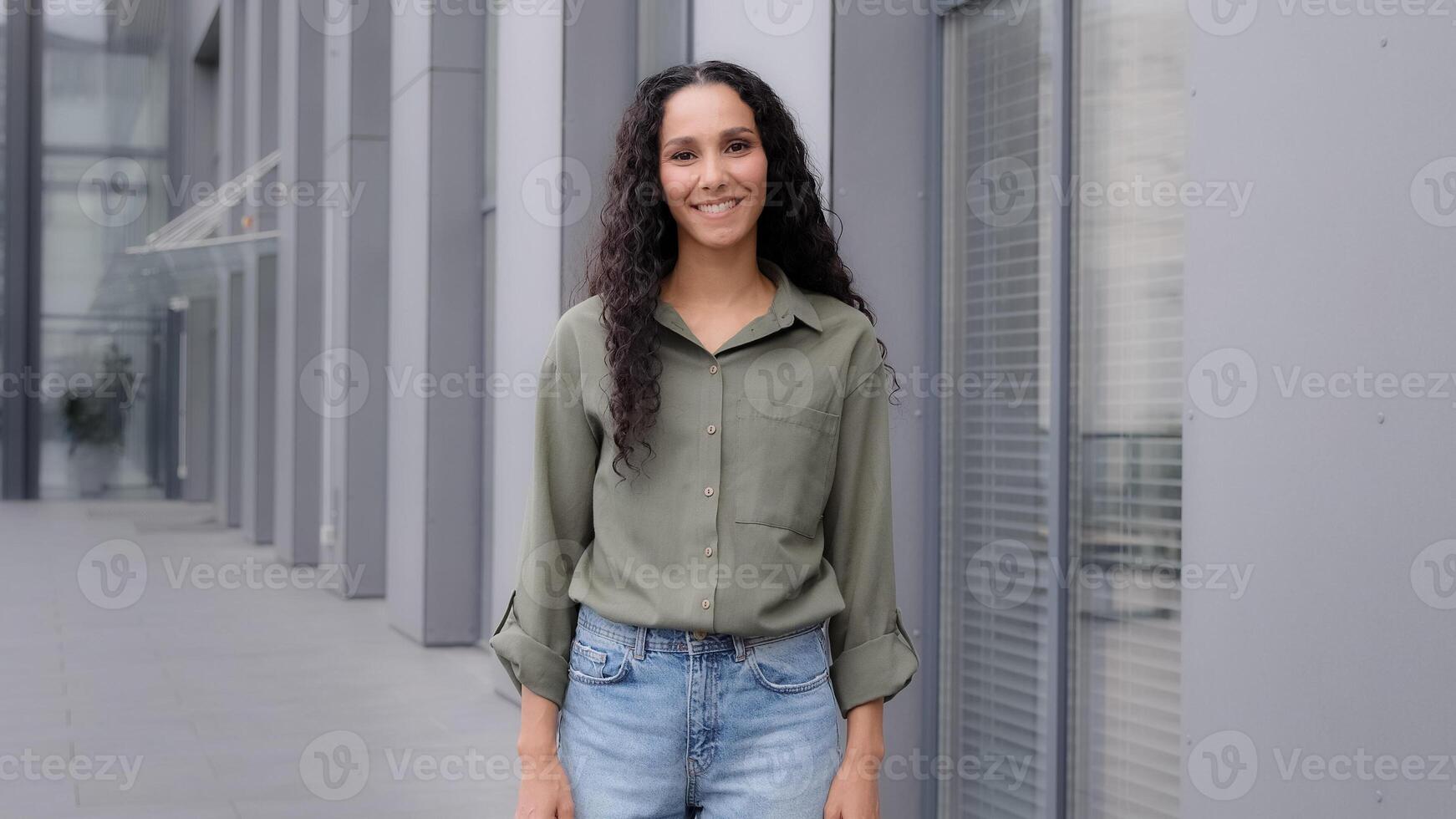 Back view from behind female with dark health curly long hair brunette woman businesswoman walker walking going in city near downtown company building turning head happy smiling looking at camera photo