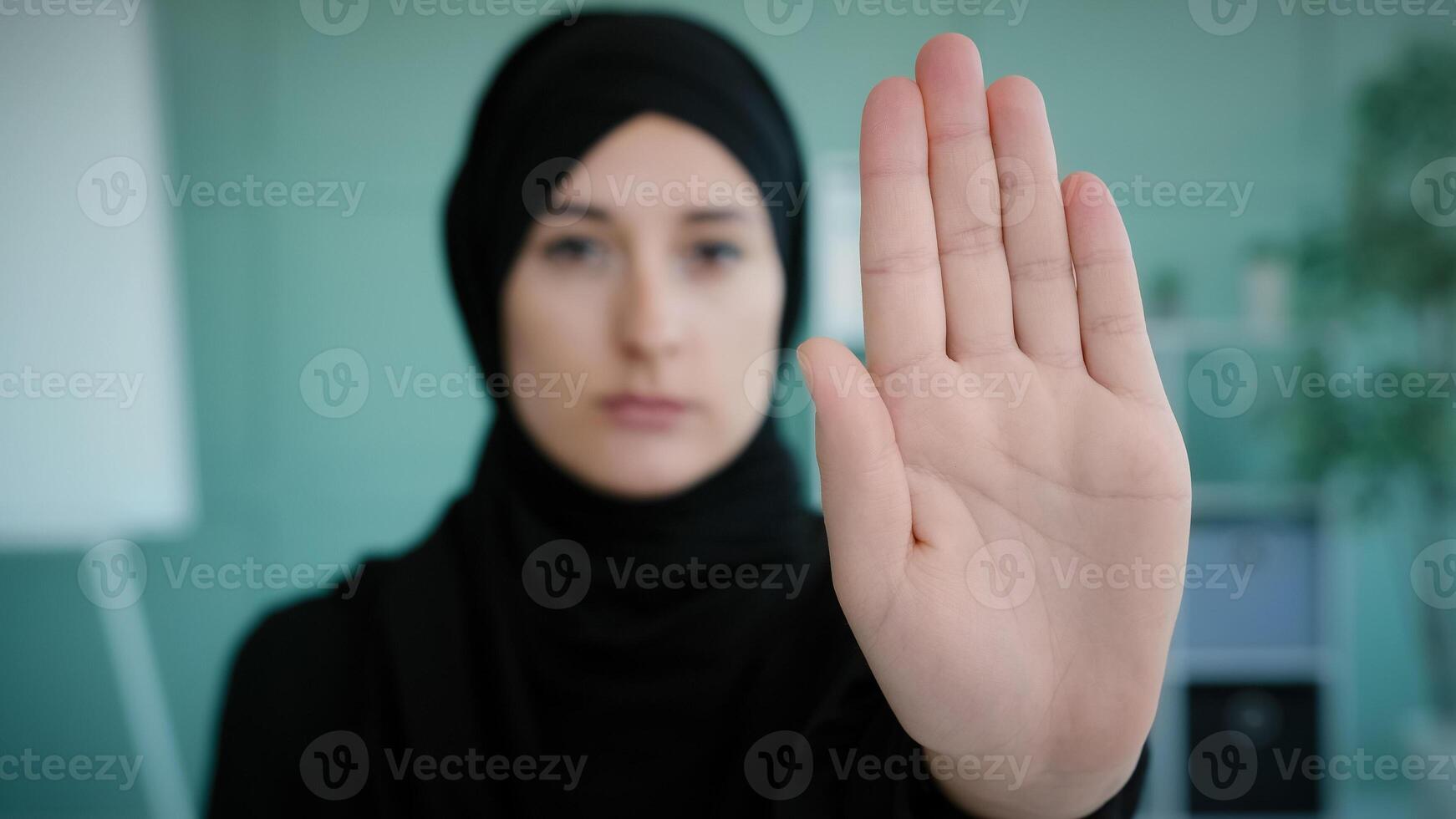 Portrait serious frustrated angry Arabian Muslim Islamic girl in black hijab upset woman looking at camera holding hand in front forbidden gesture refusal stop symbol keep distance no gesture refuse photo