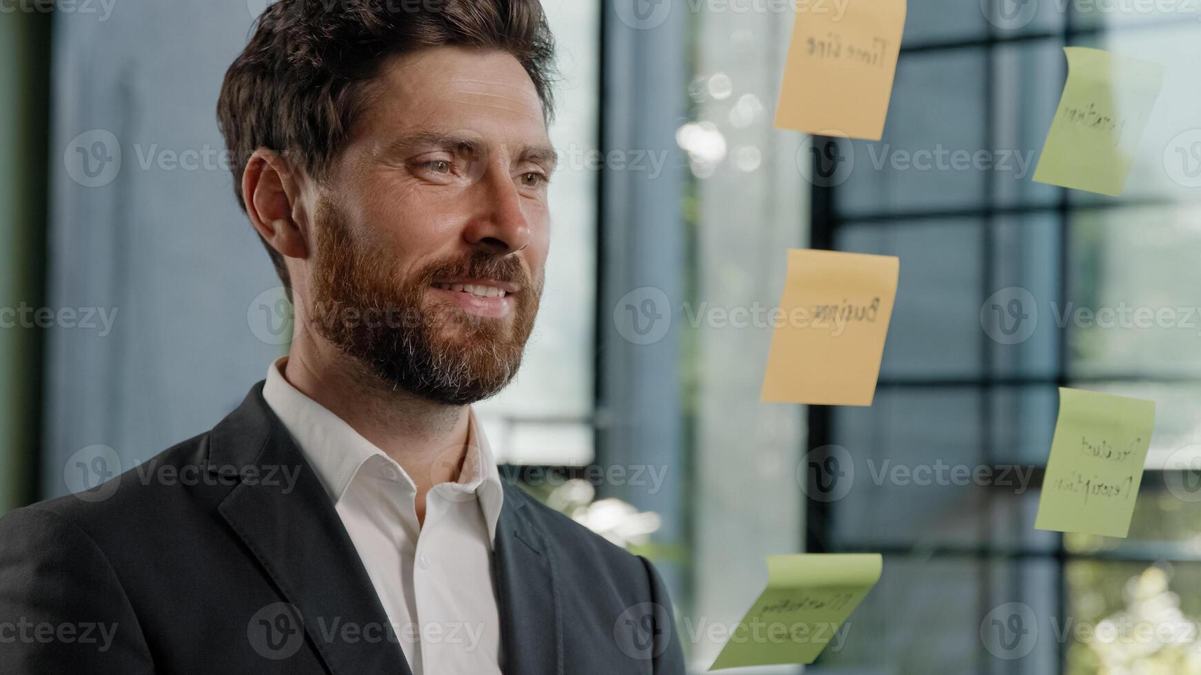 Close up 40s man busy with business strategy project management creative middle-aged businessman company CEO marketing specialist planning ideas writes sticky notes on transparent glass wall in office photo