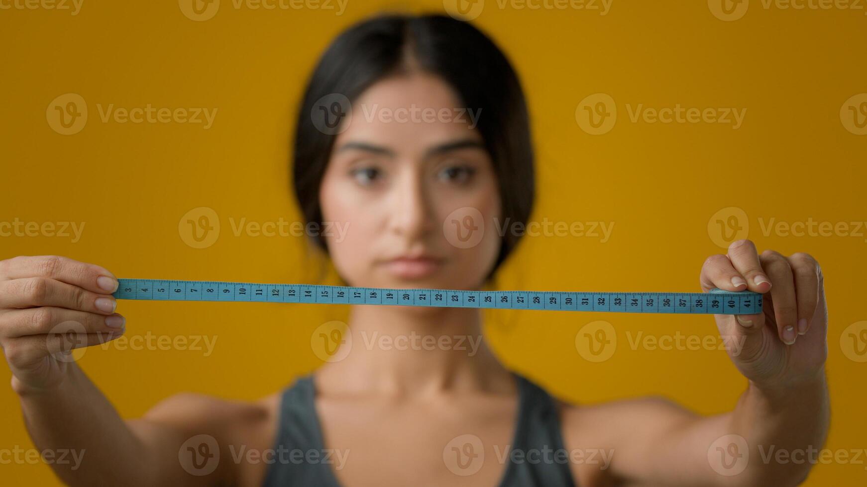 Sad upset worried Indian woman girl in yellow studio with measuring tape dissatisfied with body measure unhappy weight size shape fitness result waist fat diet bulimia anorexia unhealthy depression photo