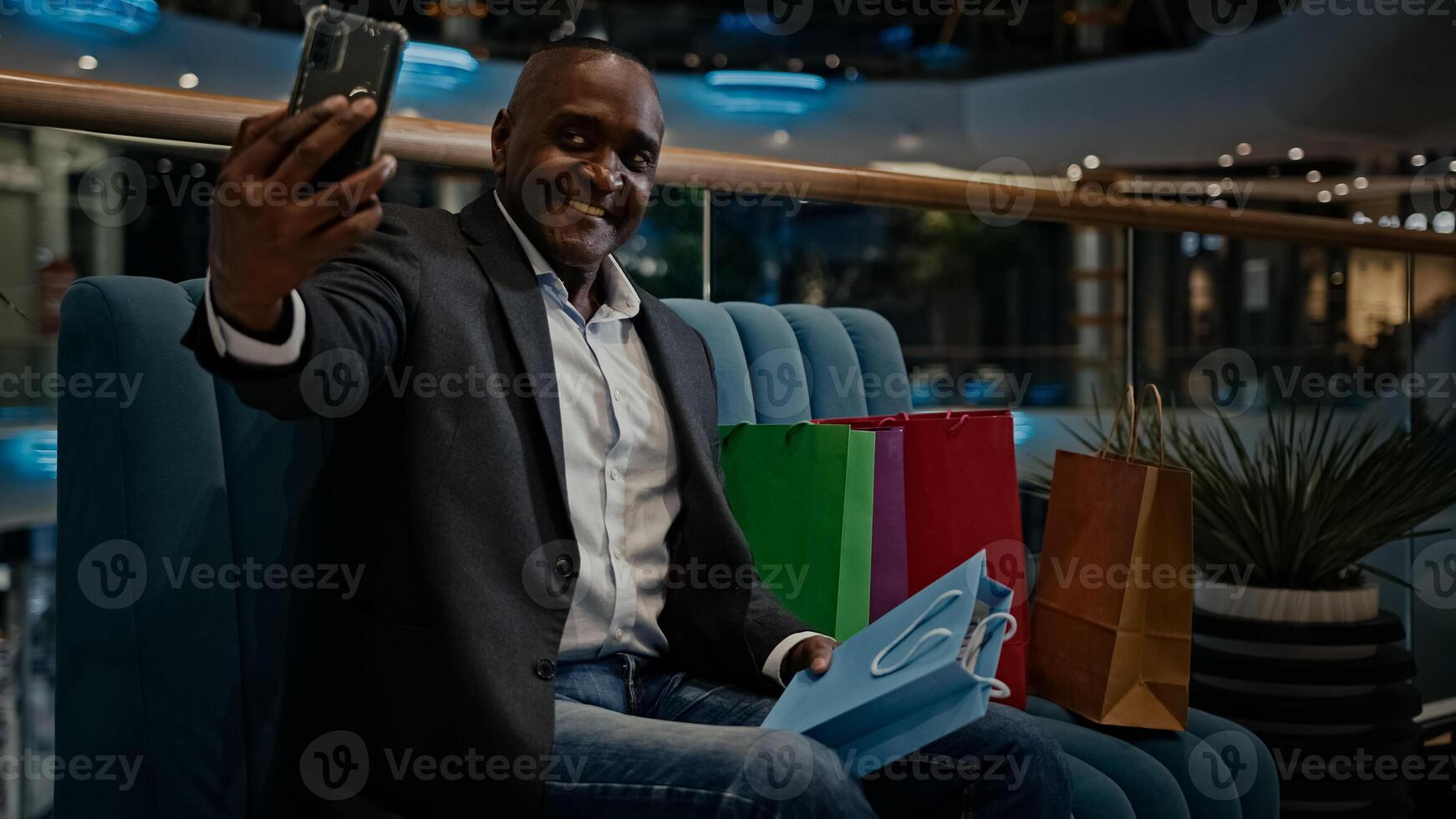 Middle-aged male African American man buyer client customer blogger influencer vlogger with shopping bags in mall call make photography with purchase smartphone photographing phone photo picture