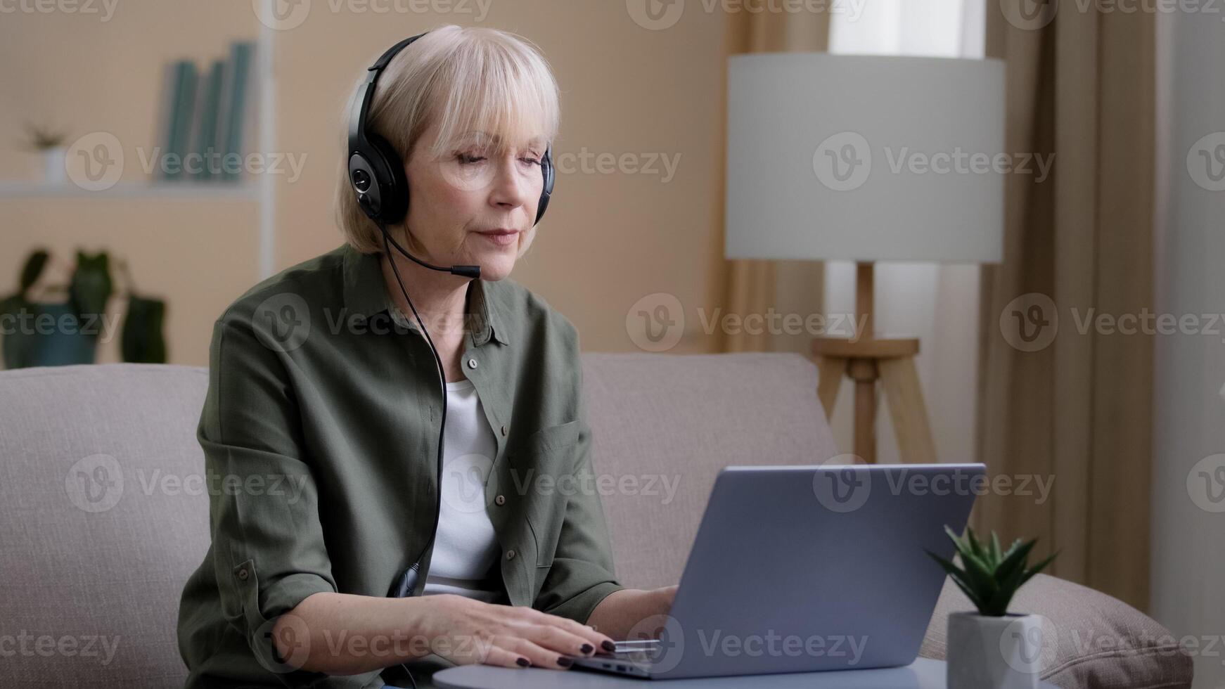 Middle aged business woman in headset talking conference distant meeting remote calling with laptop. Senior old Caucasians female online teacher communicating in virtual chat wearing headphones photo