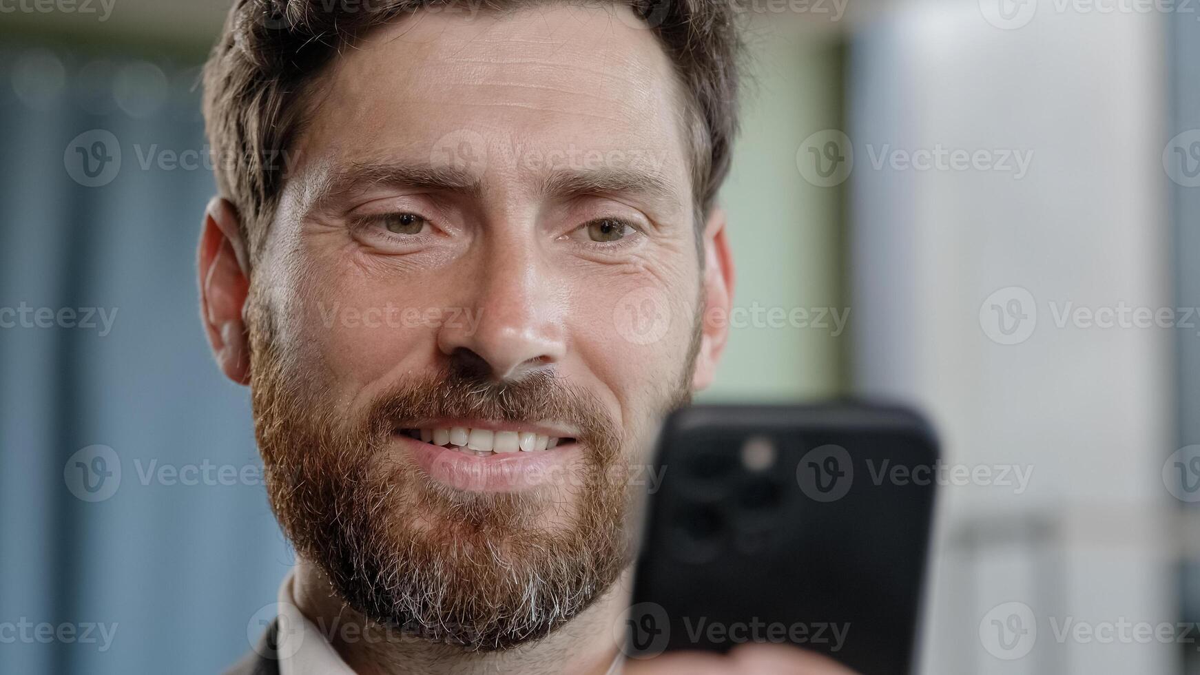 Close up head shot smiling bearded adult 40s businessman holding smartphone in office smile reading good news using online app middle-aged manager with cell phone mobile service texting corporate chat photo