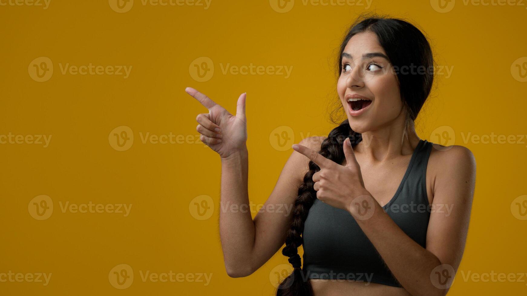 Portrait ethnic Indian sport woman girl lady female in studio yellow background pointing fingers showing on empty copy space for advertisement show aside with amaze shock recommend promotion at side photo
