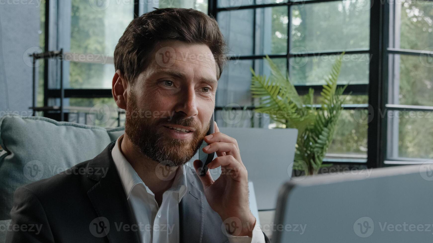 Busy bearded Caucasian adult middle-aged millennial man office worker businessman manager consulting client by telephone reading information on laptop screen looking at computer talk phone answer call photo