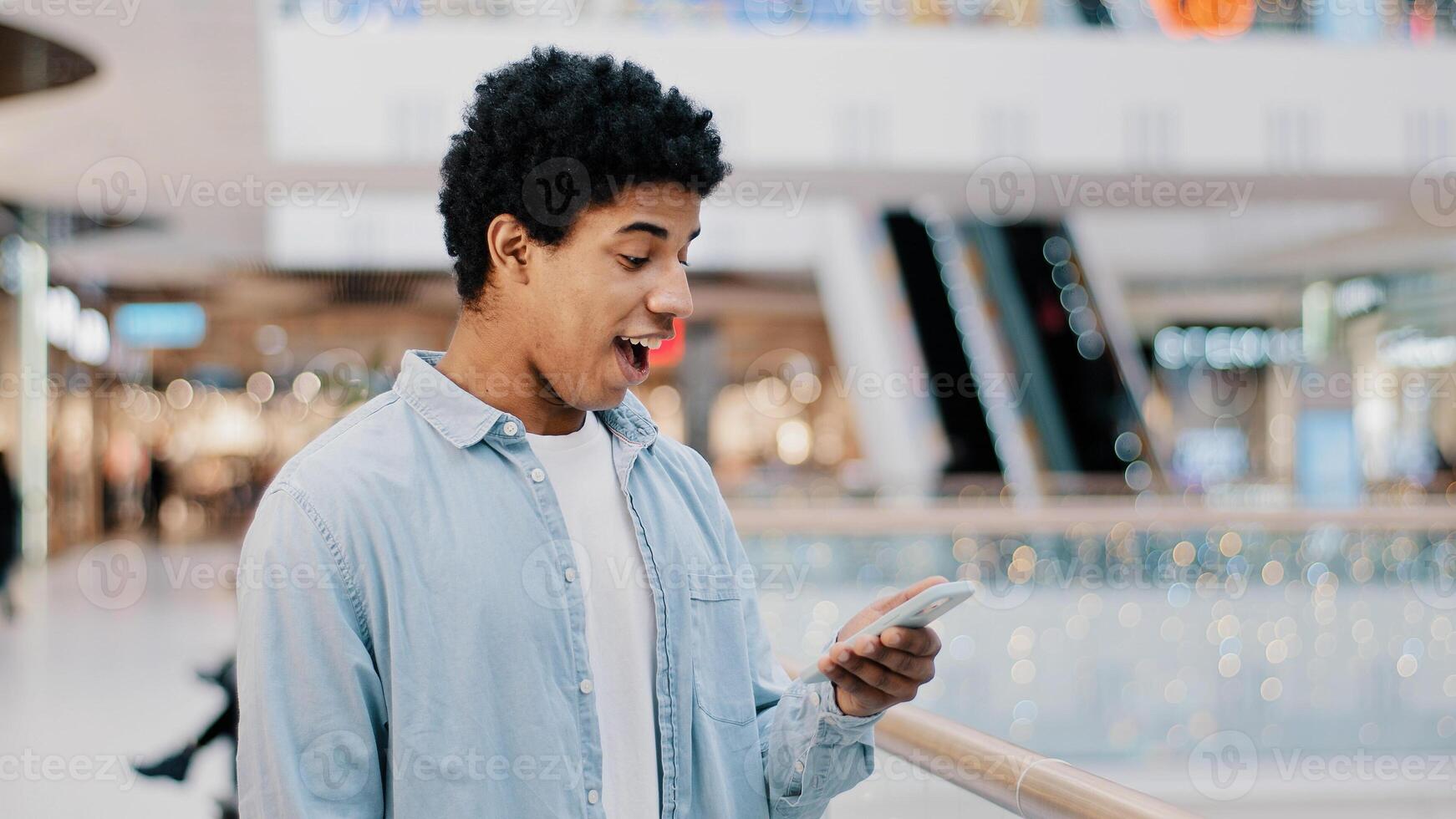 African Dominican guy surprised with phone number ringing looking at screen man answering unexpected call talking smiling laughing happy chatting cellphone friendly casual talk with good news offer photo