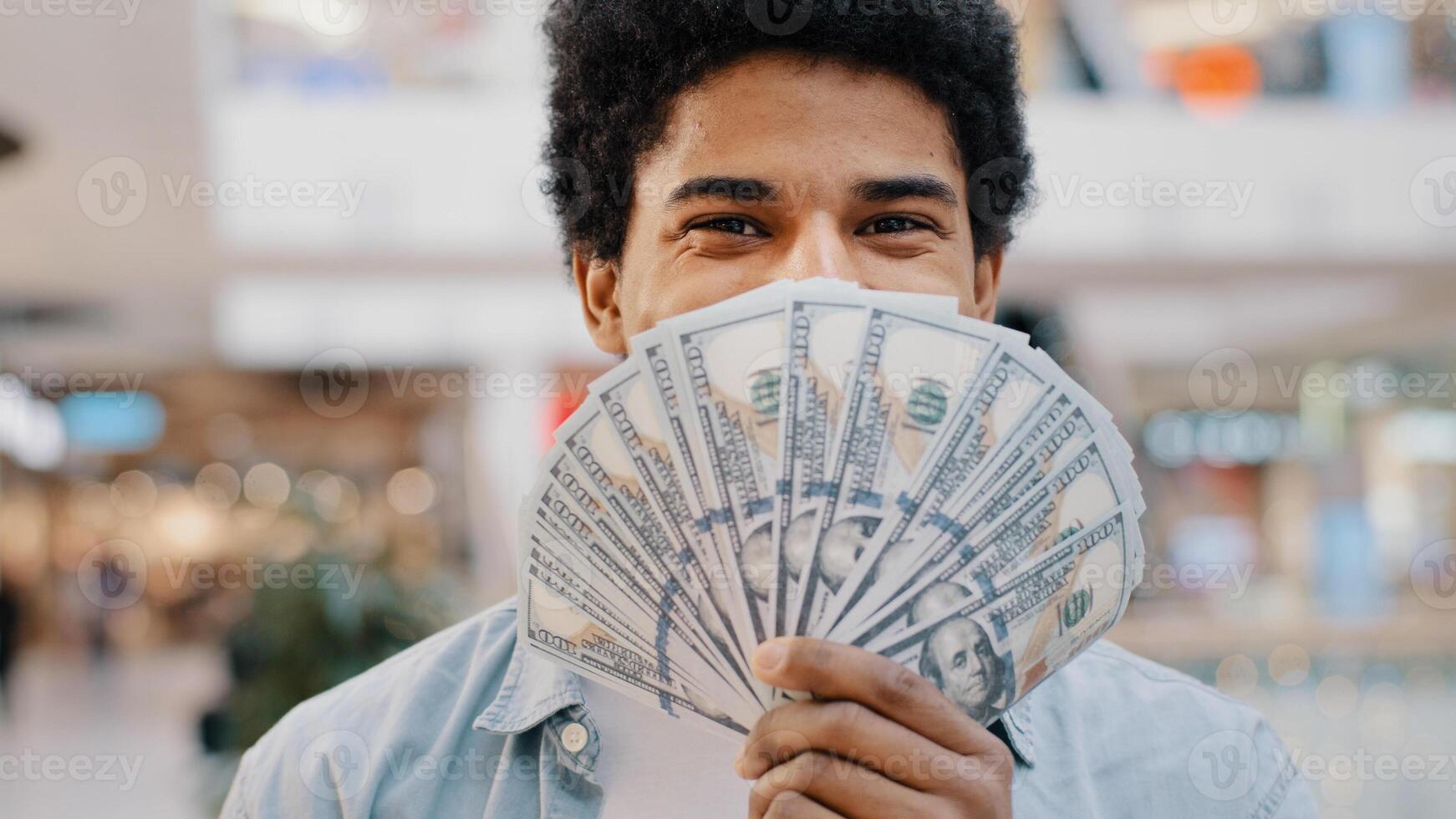 Happy wealthy successful smiling african american business man looking at camera holding fan of money hiding behind dollar banknotes showing financial profit winning salary savings loan credit cash photo
