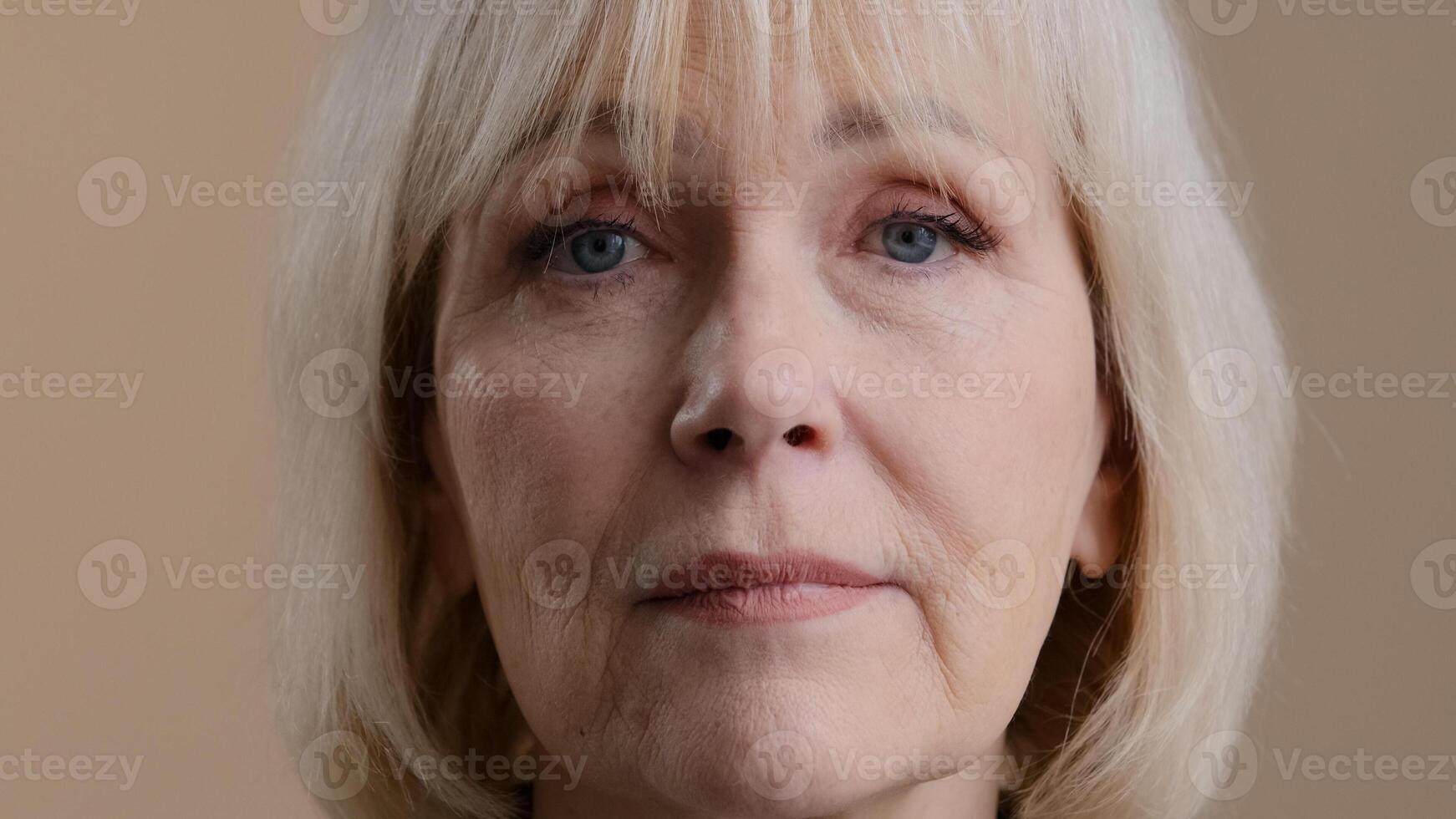 Close up female portrait in studio indoor head face wrinkled calm serious granny mature 60s woman middle-aged blonde lady senior older grandmother looking at camera wisdom skincare insurance service photo