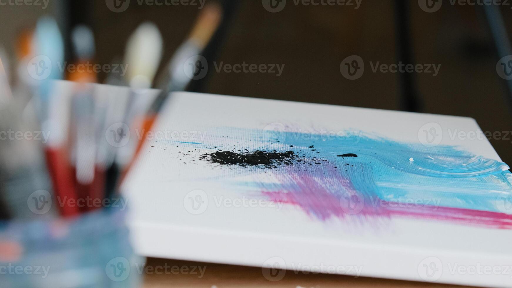 Close-up black dark paint splatters on canvas with pink and blue color picture female hand holding paint brush draws making texture creates masterpiece work of art painting preparing for exhibition photo