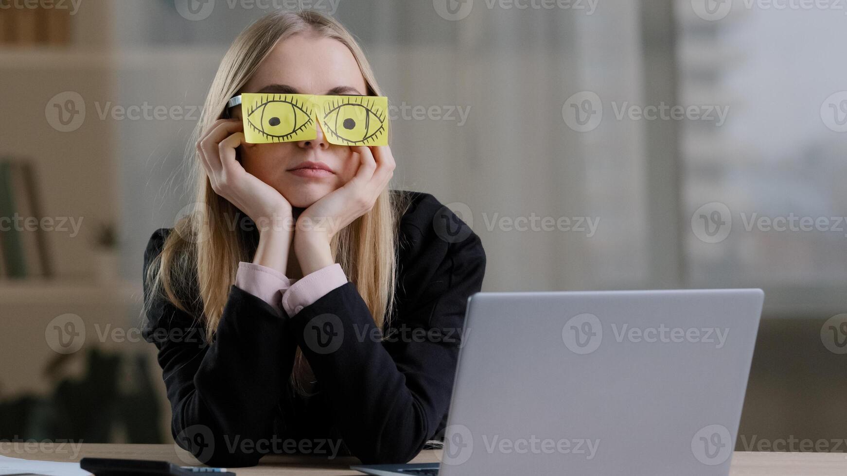 Tired sleepy funny lazy caucasian business woman with sticky notes on eyes glasses with stickers. Fatigued female worker napping at workplace sit at desk bored routine work pretends working sleeping photo